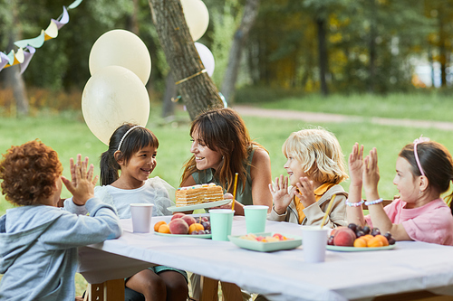 Portrait of smiling mother bringing Birthday cake to cute girl during Birthday party outdoors, copy space