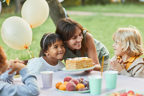 Portrait of smiling mother bringing Birthday cake to cute girl during Birthday party outdoors