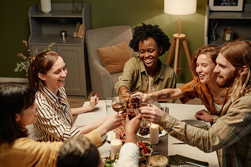 Group of happy friends toasting with drinks at dining table while celebrating the holiday together