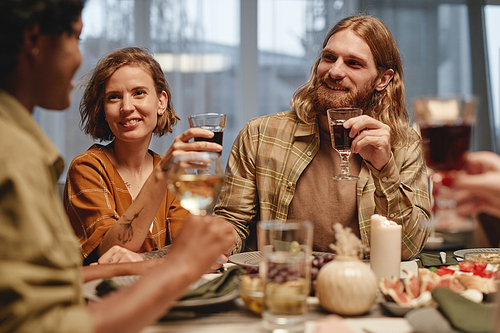 Group of young happy people drinking wine and talking to each other while they sitting at dining table at party