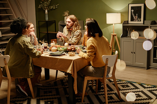 Group of friends talking to each other and eating dinner during a dinner party at home