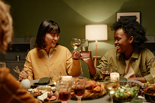 Happy young women toasting with glasses of white wine and smiling while sitting at dining table