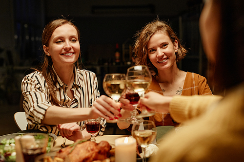 Happy young women toasting with wine and celebrating each other with holiday sitting at dining table