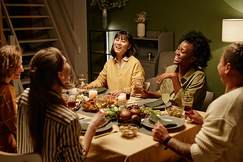 Group of young women laughing at the table during dinner party at home, they eating and drinking wine
