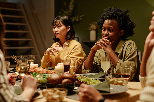 Young women sitting at dining table and listening to friends while they celebrating something at home