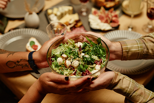 Close-up of people passing vegetable salad to each other at dining table during dinner