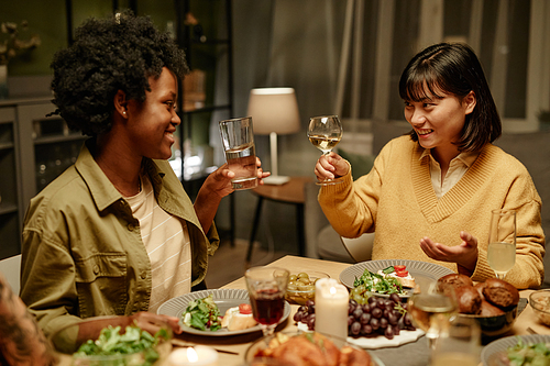 Young happy women cheering with glasses of wine at dining table at home, they celebrating the holiday