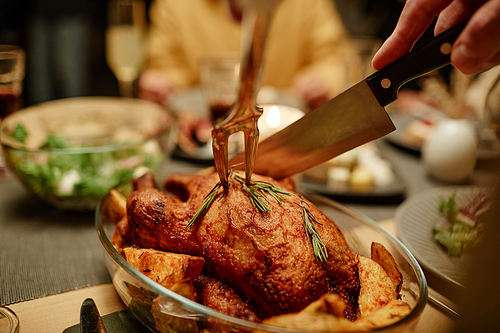 Close-up of woman cutting roast turkey with knife and fork during dinner at the table