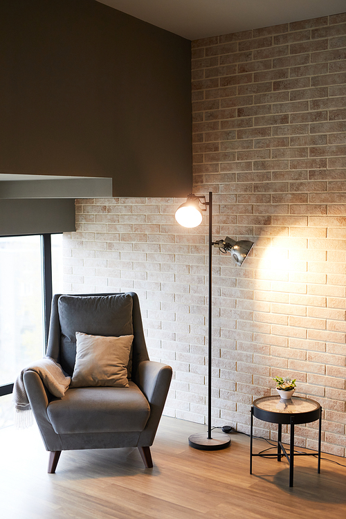 Vertical background image of minimal high back armchair with floor lamp against brick wall in loft interior, copy space