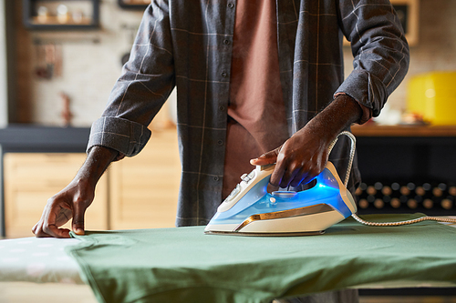 Close up of unrecognizable African-American man ironing clothes in studio apartment, bachelor lifestyle and household chores concept, copy space
