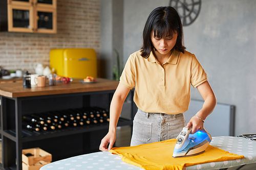 Waist up portrait of young woman ironing clothes at home and doing household chores, copy space