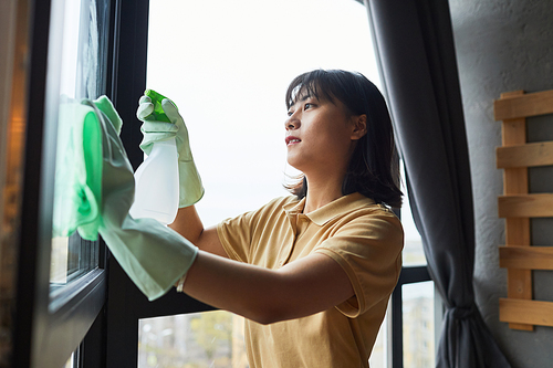 Side view portrait of young Asian woman cleaning windows at home, copy space