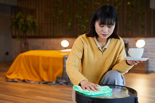 Portrait of young Asian woman cleaning coffee table in home interior, copy space