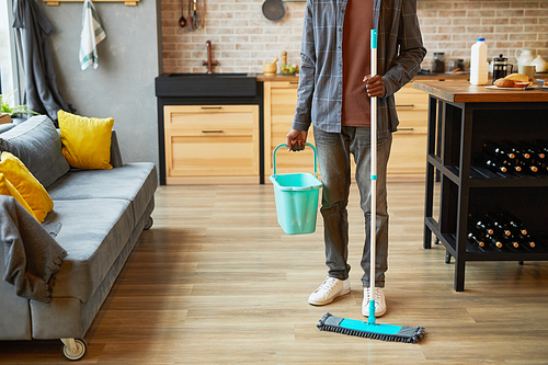 Cropped shot of young African-American man mopping floors while cleaning cozy apartment, copy space