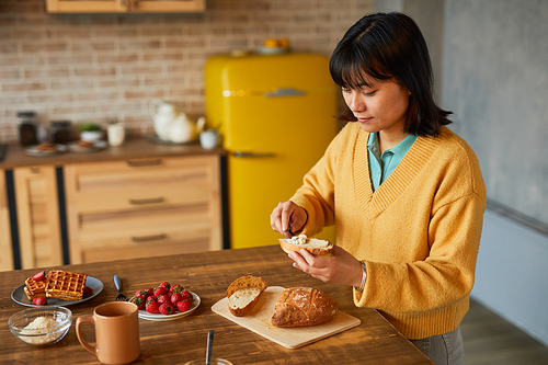 Portrait of young Asian woman making cheese sandwich while enjoying breakfast in kitchen, copy space
