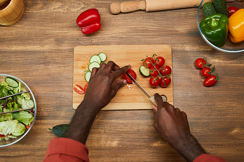 Top view close up of unrecognizable black man cutting vegetables on wooden table while cooking in kitchen, copy space