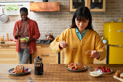 Waist up portrait of young mixed-race couple enjoying breakfast in cozy colorful kitchen, copy space