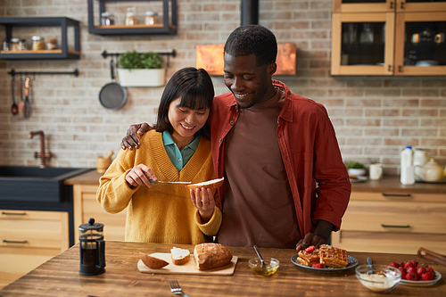 Waist up portrait of happy couple enjoying breakfast in cozy colorful kitchen, copy space