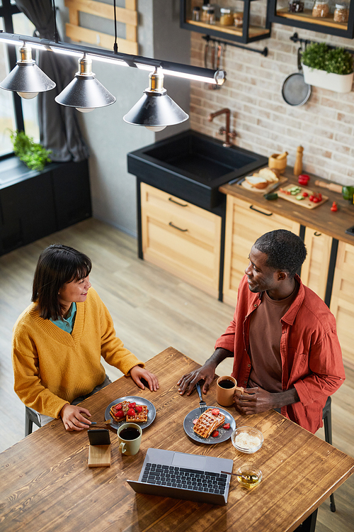 Vertical high angle portrait of couple enjoying breakfast in cozy home kitchen, copy space