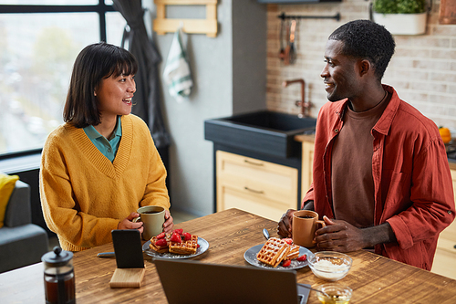 Portrait of smiling ethnic couple enjoying breakfast at table in cozy home kitchen