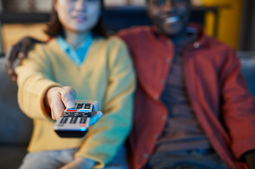 Close up of couple watching TV while relaxing on couch in blue light, focus on female hand holding remote control, copy space