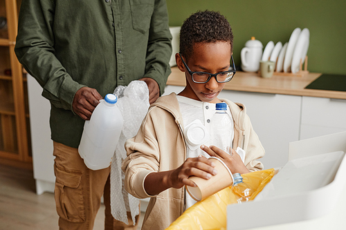 Portrait of young African-American boy sorting waste at home with father in background, copy space