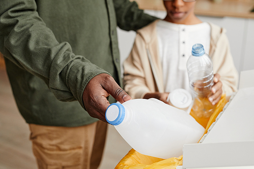 Close up of African-American father and son putting plastic in recycling bins at home, copy space