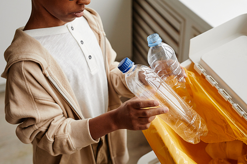 Cropped shot of African-American boy putting plastic in recycling bins at home, copy space