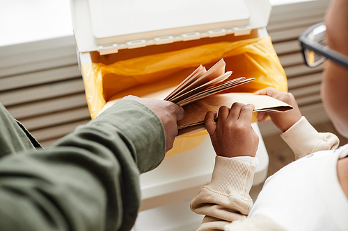 Top view close up of African-American father and son putting paper in recycling bins at home, copy space