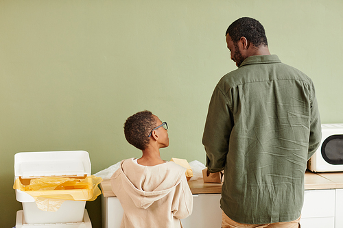 Minimal back view portrait of African-American father and son sorting household waste at home, copy space