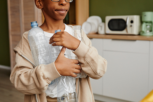 Cropped shot of teenage boy holding plastic bottles while sorting household waste at home, copy space