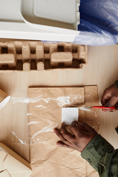 Close up of African-American man preparing household waste for recycling and cutting out labels, copy space