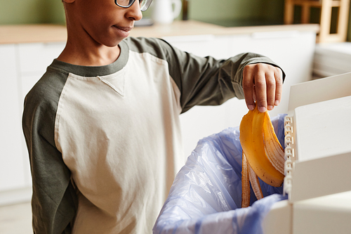 Side view close up of boy sorting household waste at home and putting banana peel in recycling bin, copy space