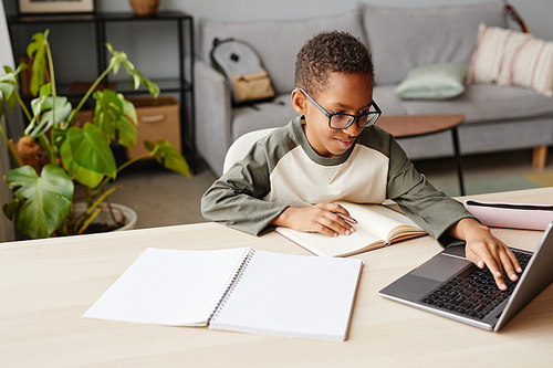 Portrait of smiling African-American boy wearing glasses using laptop while studying at home, homeschooling concept, copy space