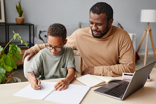 Portrait of African-American father helping son with homeschooling while studying at home, copy space
