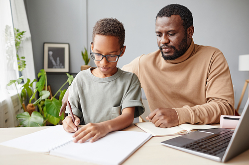 Portrait of caring African-American father helping son with homeschooling while studying at home, copy space