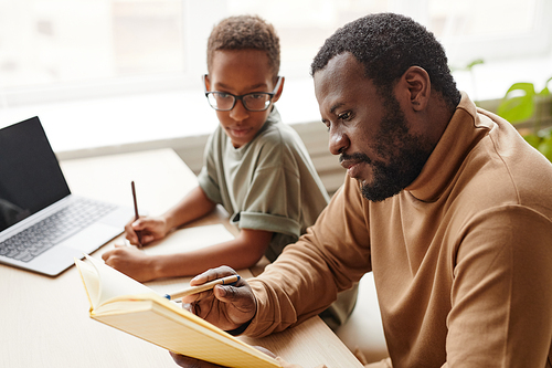 Side view portrait of caring father helping son with homeschooling while studying at home, copy space