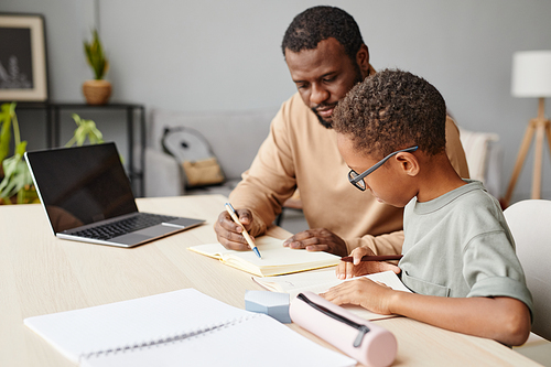 Portrait of caring father helping son with homework while studying at home, copy space