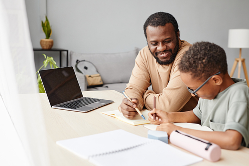 Portrait of smiling African-American father helping son with homework while studying at home, copy space