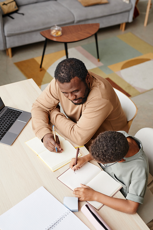 High angle portrait of caring father helping son with homework while studying at home, copy space
