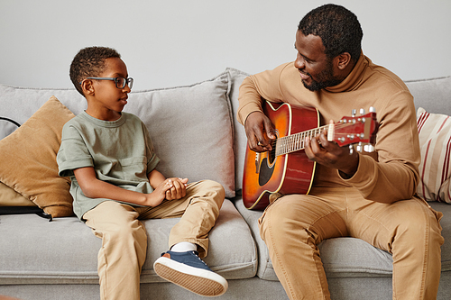 Portrait of smiling African-American father teaching son to play guitar and musical instruments, copy space