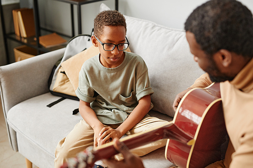 Portrait of young African-American boy learning to play guitar at home with father, copy space