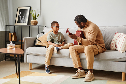 Full length portrait of African-American father teaching son to play guitar and musical instruments, copy space