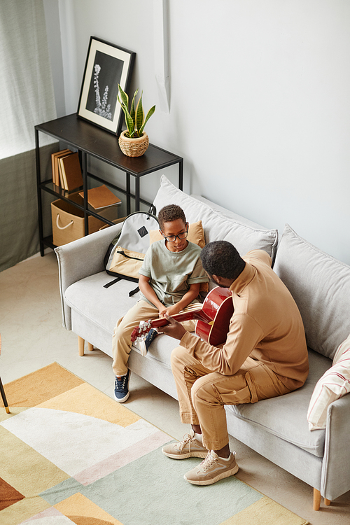 Vertical high angle portrait of African-American father teaching son to play guitar and musical instrument