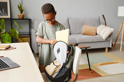 Portrait of young African-American boy packing backpack at home, copy space