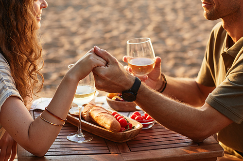 Close up of young couple holding hands at picnic outdoors while enjoying romantic date in sunlight, copy space