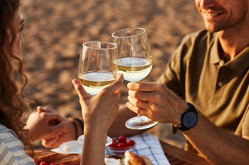 Close up of young couple drinking wine outdoors on beach while enjoying romantic date at sunset, copy space