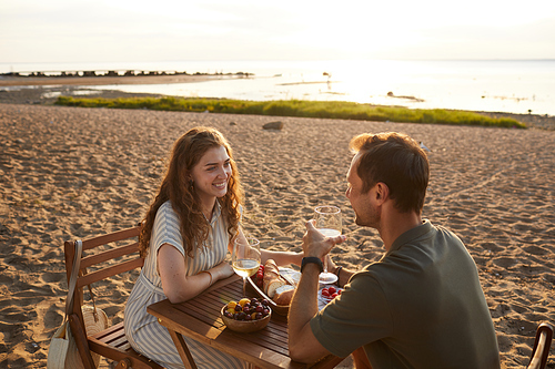 Portrait of happy young couple at picnic outdoors while enjoying romantic date on beach at sunset, copy space