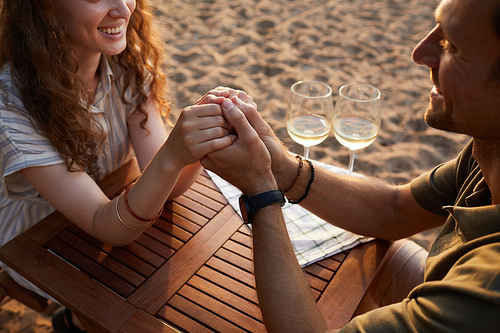 Close up of happy young couple holding hands at picnic outdoors while enjoying romantic date on beach, copy space