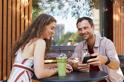 Portrait of happy couple looking at smartphone screen at outdoor cafe while enjoying date in Summer, copy space